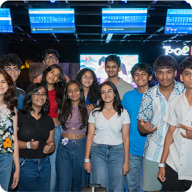 A group of young people smiling and posing together in front of a brightly lit bowling alley entrance