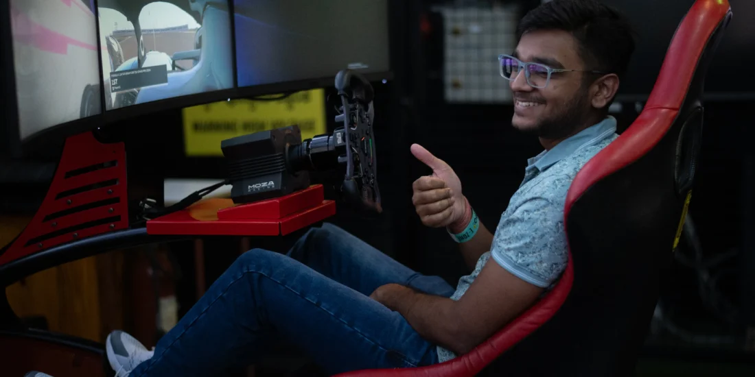 A man sitting in a racing simulator, smiling and giving a thumbs up, indicating enjoyment and excitement