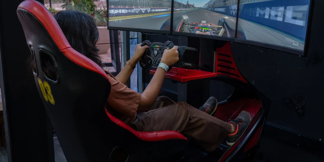 A woman is focused on playing a racing game using a simulator, with a steering wheel and screen in front of her