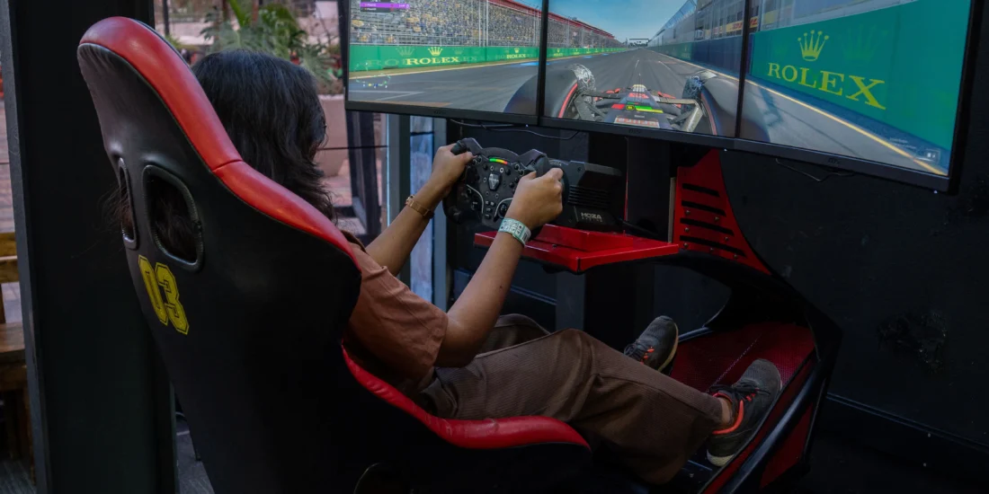 A woman is focused on playing a racing game using a simulator, with a steering wheel and screen in front of her