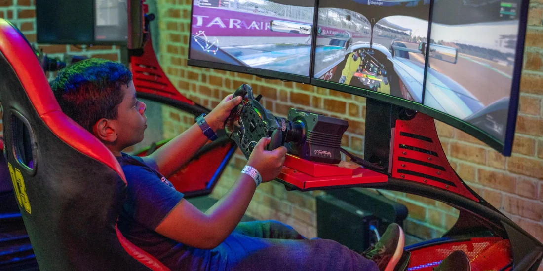 A young boy is focused on playing a racing game using a racing simulator, with a steering wheel and pedals