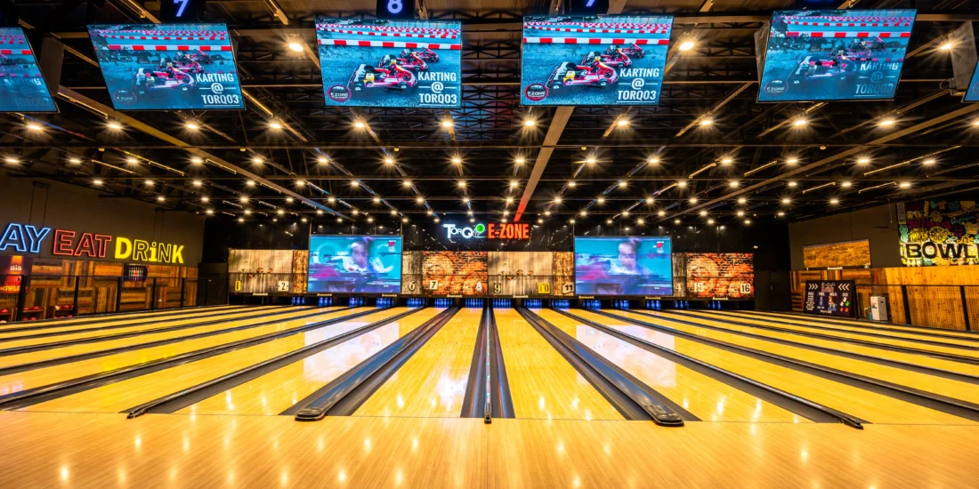 A vibrant bowling alley scene with several screens highlighting bowling scores and action
