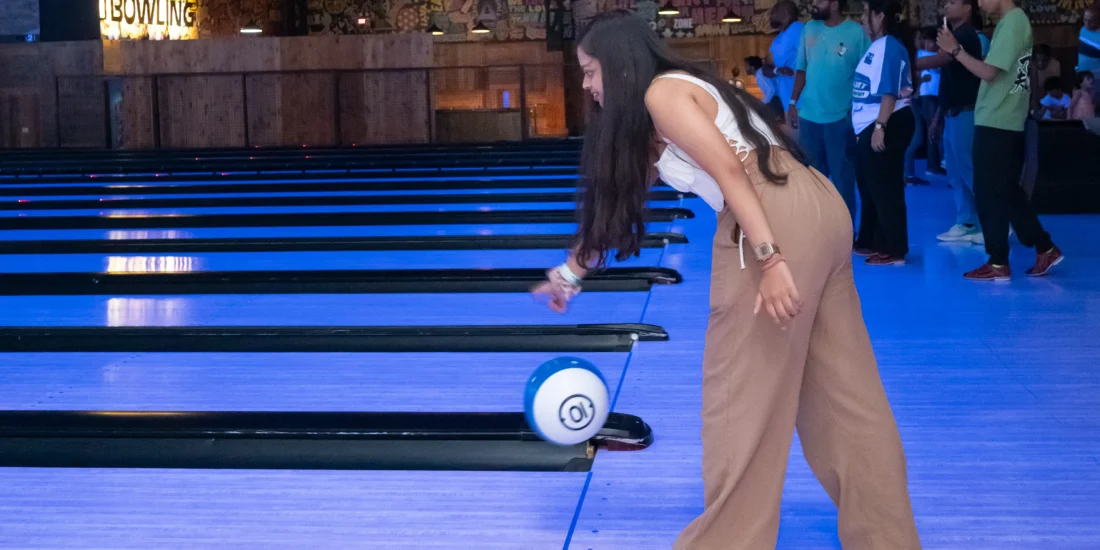 A woman in a bowling alley rolls a bowling ball down the lane, aiming for the pins at the end
