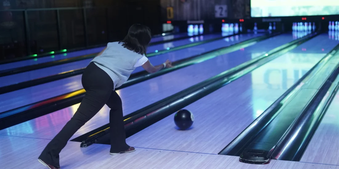 A woman in a bowling alley prepares to roll a bowling ball down the lane, focused on her target