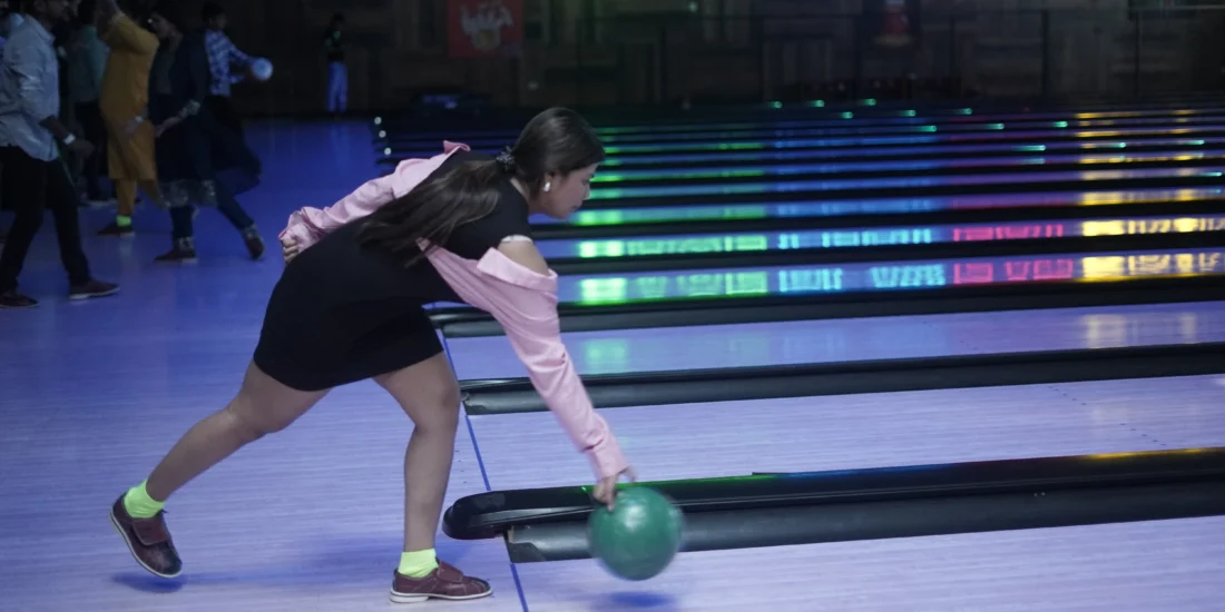 A woman bowls on a brightly lit lane, surrounded by vibrant neon lights creating a lively atmosphere