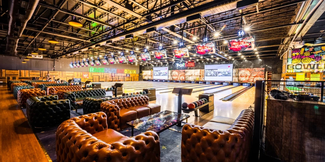 Interior view of a bowling alley, featuring multiple lanes, bowling balls, and players enjoying the game