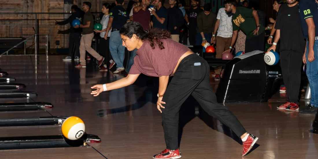 A woman bowls in a lively bowling alley, surrounded by other players enjoying the game