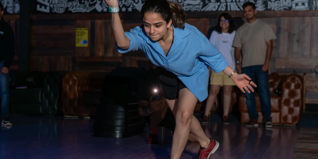 A woman in a blue shirt bowls with a green ball, focusing intently on her aim at the bowling lane
