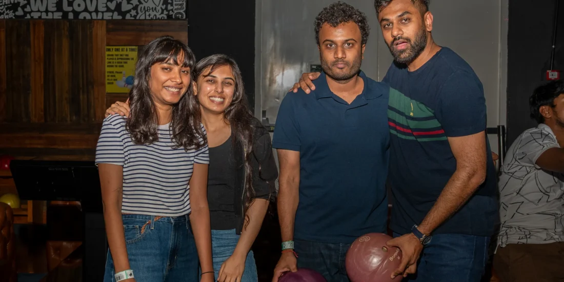 A group of friends smiling and posing together for a photo in a vibrant bowling alley setting