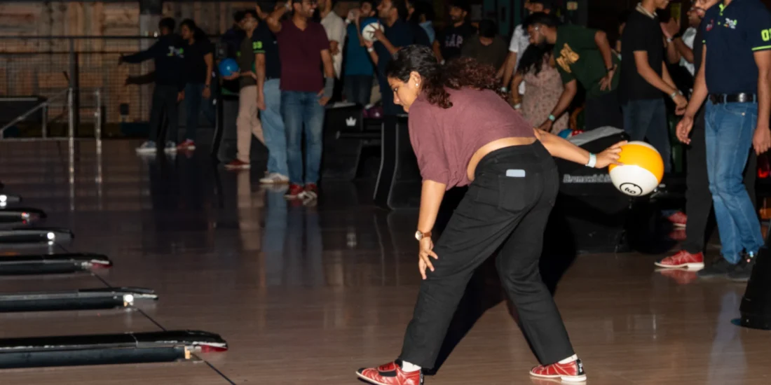 In a bowling alley, a woman wearing a red shirt is poised to bowl, concentrating on her next move