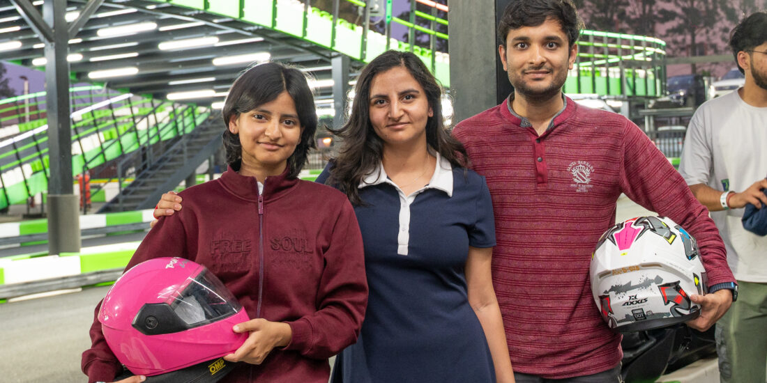 A man and two women posing together, smiling in a casual outdoor setting carring helment after Go Karting