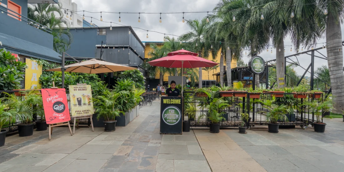 A city restaurant featuring outdoor tables with umbrellas, surrounded by urban buildings and bustling street activity