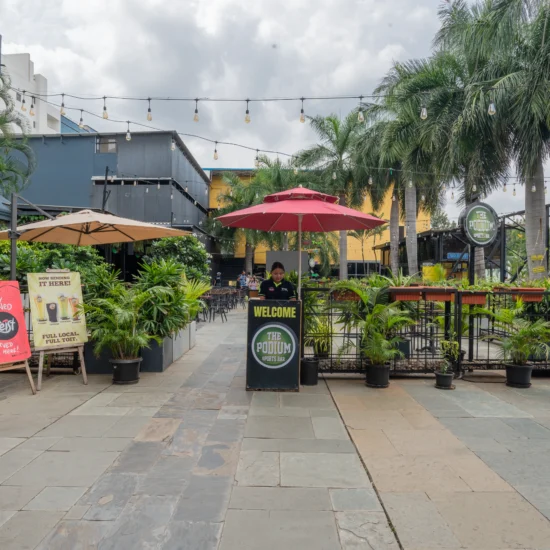 A city restaurant featuring outdoor tables with umbrellas, surrounded by urban buildings and bustling street activity
