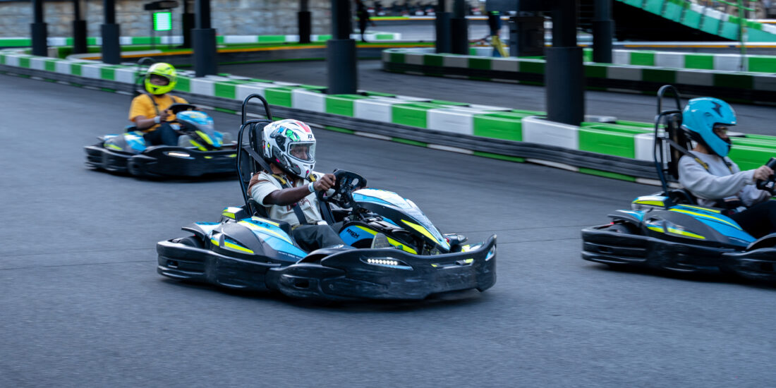 Three individuals racing go-karts on a track, showcasing excitement and competition in a vibrant outdoor setting