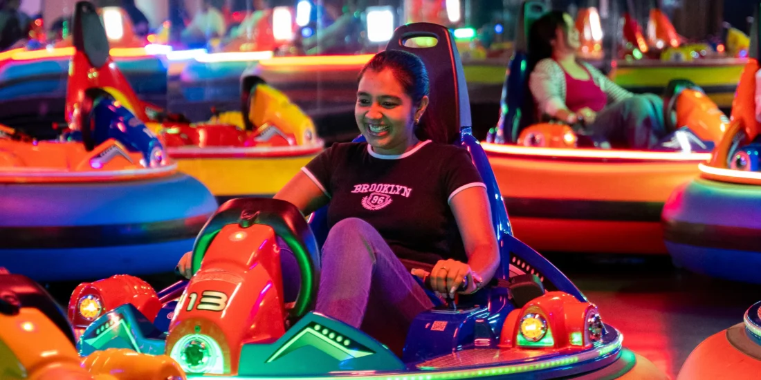 A woman enjoys riding in bumper cars at an amusement park, smiling as she navigates the colorful attractions