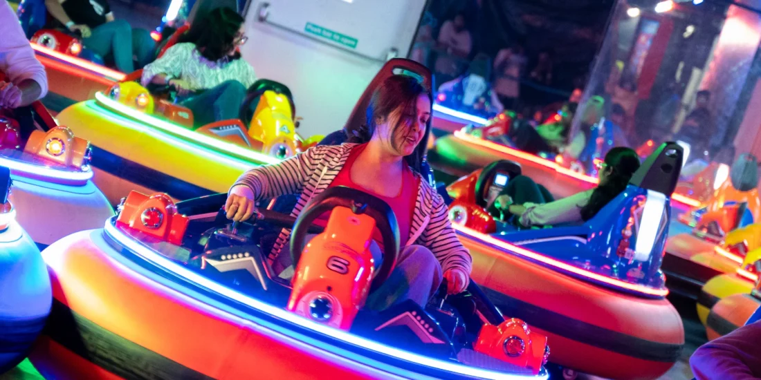 Several individuals riding bumper cars in an amusement park, surrounded by vibrant lights and joyful atmosphere